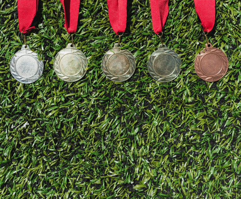 Bild uppifrån på medaljer i olika valörer liggandes på gräsplan