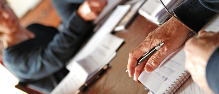 Människor på ett möte som skriver ner anteckningar på ett papper