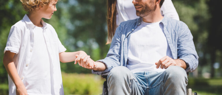 En pojke håller hand med en man som sitter i rullstol