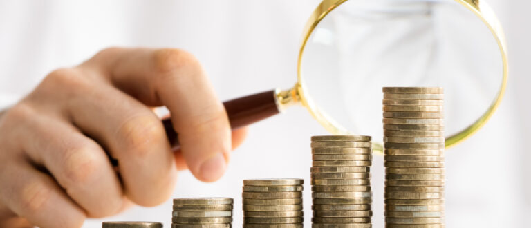 En hand som håller i ett förstoringsglas över några högar av mynt