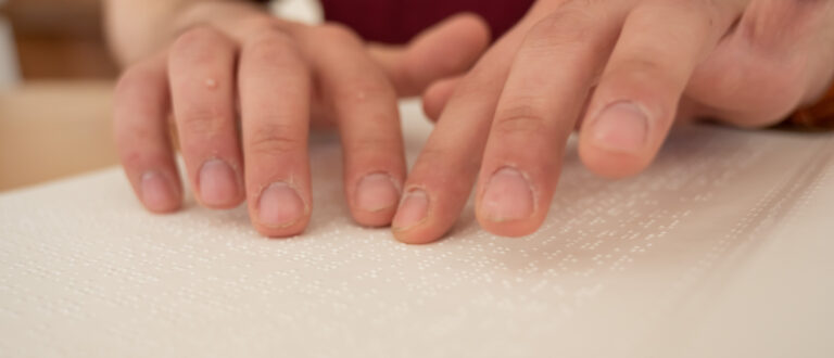 Man ser händerna på en blind person som läser en punktskrift