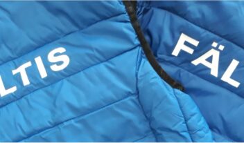 Närbild på två blå vadderade västar där det står Fältis på ryggen i vitt