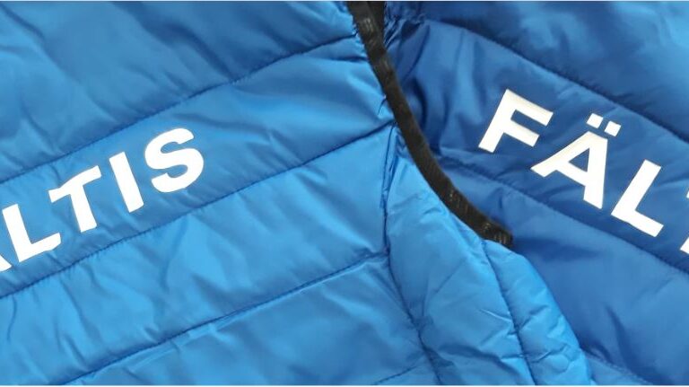 Närbild på två blå vadderade västar där det står Fältis på ryggen i vitt